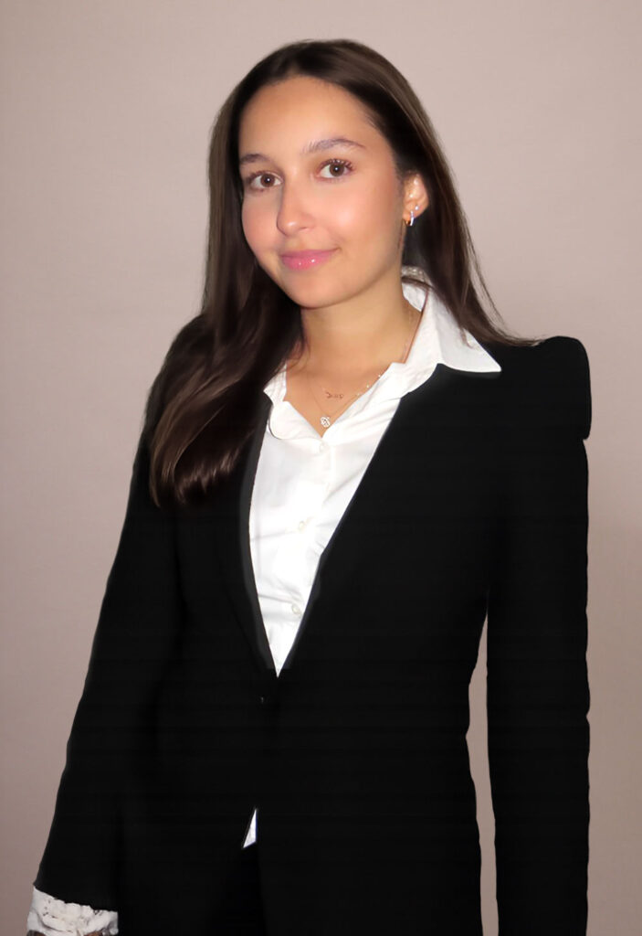 Portrait of a young woman in a black blazer and white shirt, smiling at the camera against a neutral background.